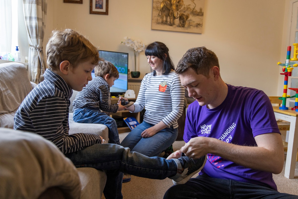 Young male Home-Start volunteer helps put shoes on children